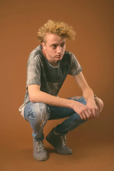 Hagerer junger Mann mit lockigem Haar vor braunem Hintergrund — Stockfoto