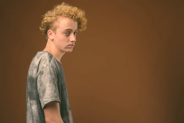 Kahverengi arka plan karşı kıvırcık saçlı sıska genç adam — Stok fotoğraf