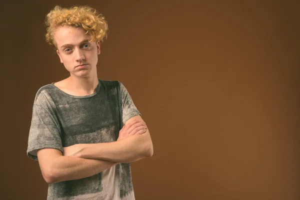 Skinny young man with curly hair against brown background
