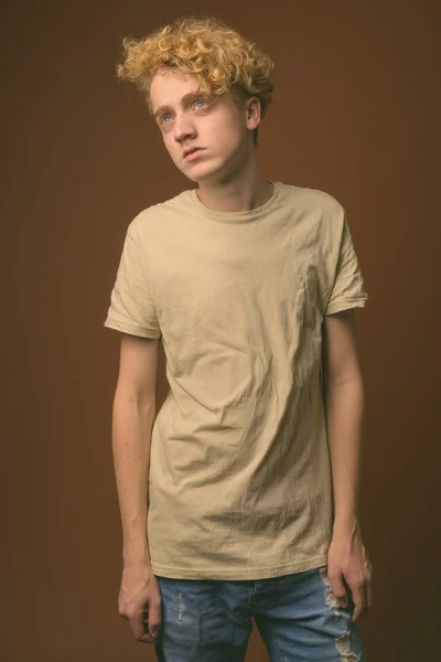 Hagerer junger Mann mit lockigem Haar vor braunem Hintergrund — Stockfoto
