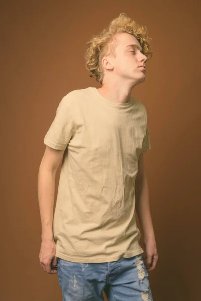 Тощий молодой человек с вьющимися волосами на коричневом фоне — стоковое фото