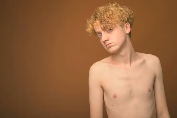 Hubený mladý muž s kudrnatými vlasy bez trička na hnědém pozadí — Stock fotografie