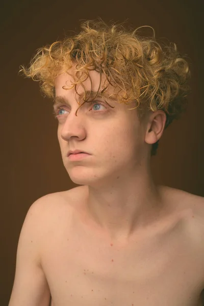 Тощий молодой человек с вьющимися волосами без рубашки на коричневом фоне — стоковое фото