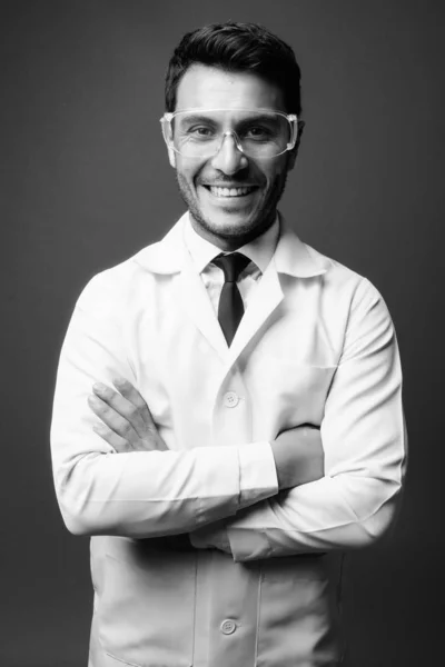 スタジオショットの若いですハンサムなヒスパニック系男性医師として科学者として保護眼鏡に対する灰色の背景に黒と白 — ストック写真