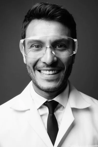 スタジオショットの若いですハンサムなヒスパニック系男性医師として科学者として保護眼鏡に対する灰色の背景に黒と白 — ストック写真
