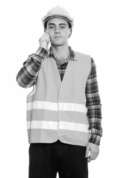 Studio shot of young man construction worker standing while talking on mobile phone — 스톡 사진