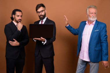 Üç çok ırklı sakallı iş adamı kahverengi arka planda karşı karşıya.