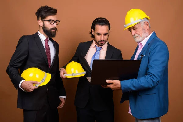 Tres hombres de negocios barbudos multi étnicos juntos contra el fondo marrón — Foto de Stock