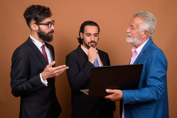 Három többnemzetiségű szakállas üzletember, barna háttérrel — Stock Fotó