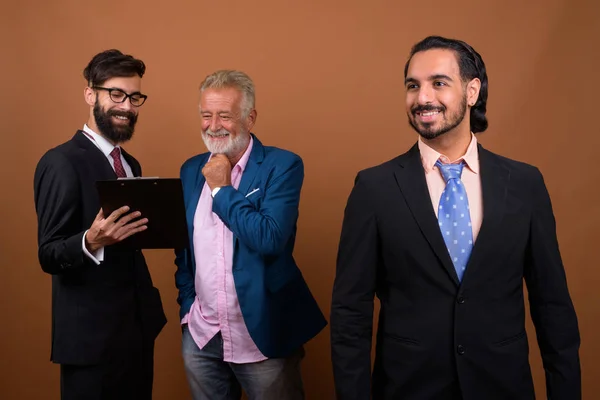 Tres hombres de negocios barbudos multi étnicos juntos contra el fondo marrón — Foto de Stock