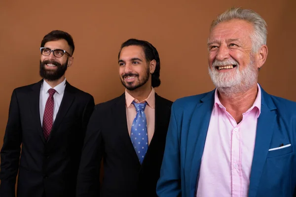 Tres hombres de negocios barbudos multi étnicos juntos contra el fondo marrón — Foto de Stock