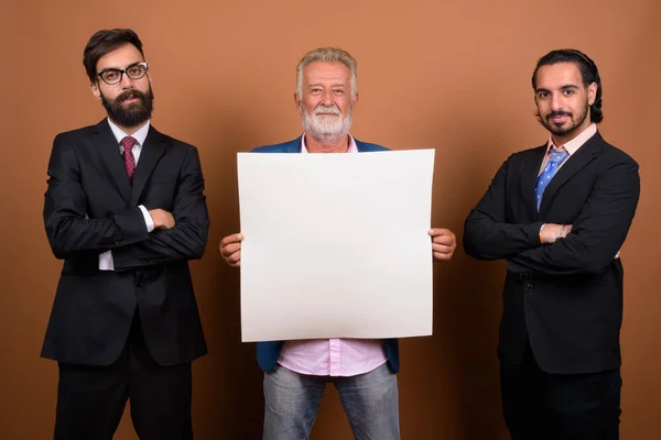 Three multi ethnic bearded businessmen together against brown background