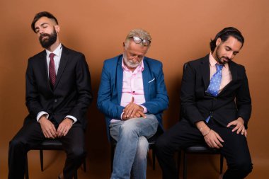 Üç çok ırklı sakallı iş adamı kahverengi arka planda karşı karşıya.