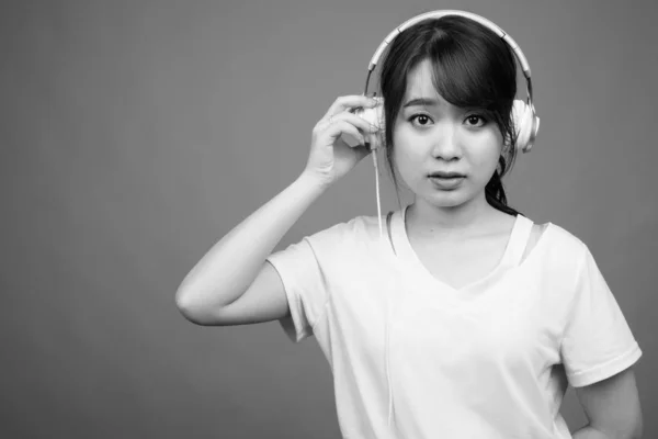 Зйомки Молодої Красивої Азіатської Жінки Яка Слухає Музику Сірому Фоні — стокове фото