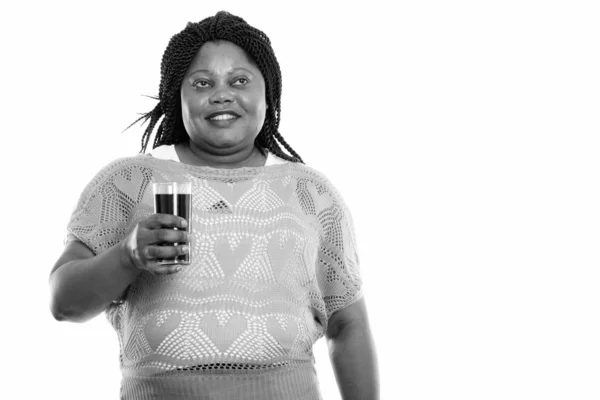 Studio záběr šťastné tlusté černošky africké ženy usmívat a přemýšlet, zatímco drží sklenici limonády — Stock fotografie