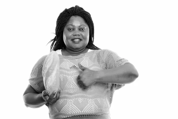 Studio záběr šťastný tlustý černošky africký žena s úsměvem při držení chleba a dávat palec nahoru — Stock fotografie