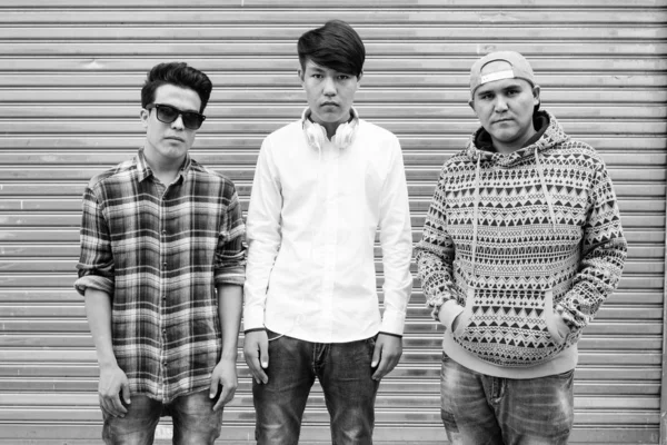 stock image Portrait of three young Asian men standing against warehouse together in the streets outdoors in black and white