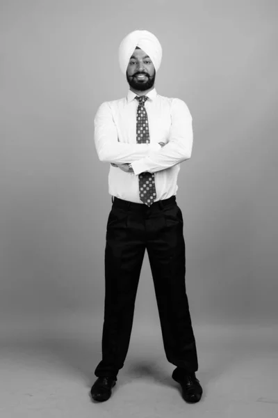 Studio shot of young bearded Indian Sikh businessman with turban against gray background in black and white