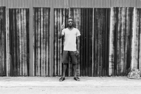 Νεαρός μαύρος Αφρικανός στέκεται ενώ δείχνει το δάχτυλο στον παλιό σκουριασμένο τοίχο. — Φωτογραφία Αρχείου
