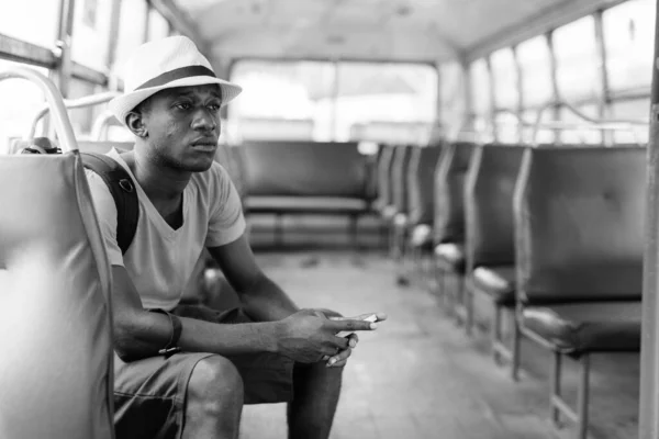 Νεαρός Αφρικανός τουρίστας που χρησιμοποιεί κινητό τηλέφωνο και οδηγεί το λεωφορείο — Φωτογραφία Αρχείου