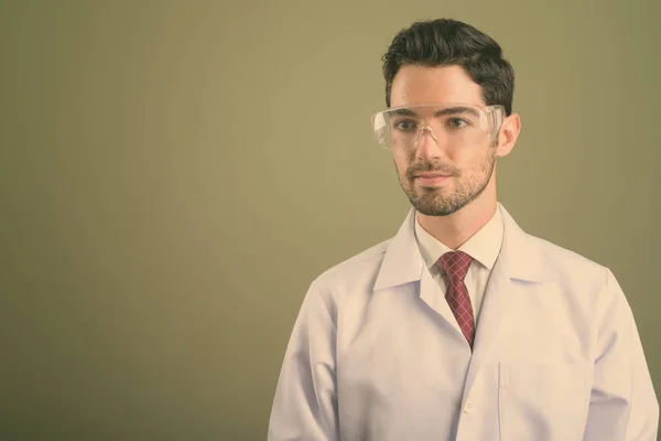 Jovem bonito homem médico vestindo óculos de proteção contra fundo colorido — Fotografia de Stock