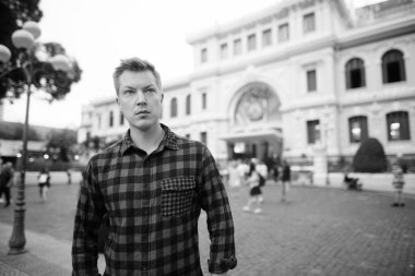 Portrait of young handsome tourist man exploring Ho Chi Minh city in Vietnam in black and white
