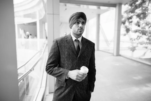 Portrait of young handsome Indian Sikh businessman wearing turban while exploring the city in black and white