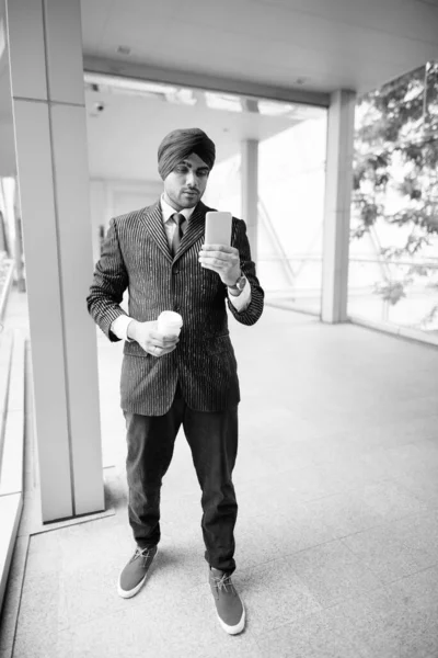 Portrait of young handsome Indian Sikh businessman wearing turban while exploring the city in black and white