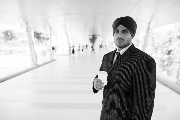 Portrait of young handsome Indian Sikh businessman wearing turban while exploring the city in black and white