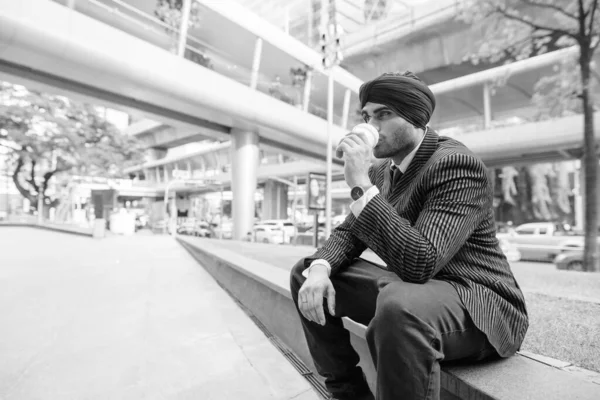 Portrait of young handsome Indian Sikh businessman wearing turban while exploring the city in black and white