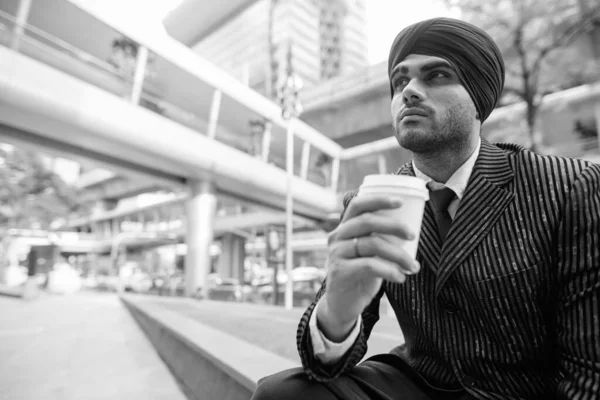 Portrait of young handsome Indian Sikh businessman wearing turban while exploring the city in black and white