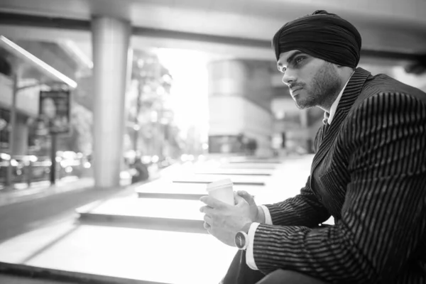 Portrait of young handsome Indian Sikh businessman wearing turban while exploring the city in black and white