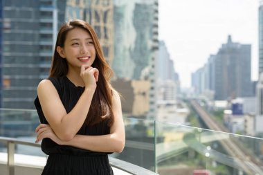 Portrait of young beautiful Asian businesswoman against view of the city