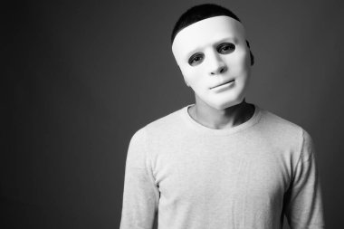 Siyah beyaz arka planda beyaz maske takan genç adamın stüdyo fotoğrafı.