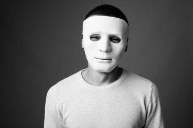 Siyah beyaz arka planda beyaz maske takan genç adamın stüdyo fotoğrafı.