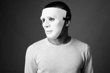 Siyah beyaz arka planda beyaz maske takan genç adamın stüdyo fotoğrafı.