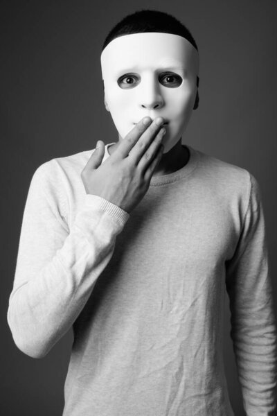 Studio shot of young man wearing white mask against gray background in black and white