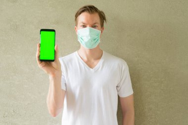 Portrait of young Scandinavian man wearing mask for protection from corona virus outbreak against concrete wall