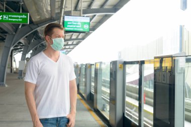 Portrait of young Scandinavian man wearing mask for protection from corona virus outbreak at the sky train station