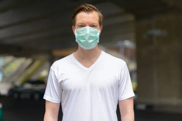 Portrait of young Scandinavian man wearing mask for protection from corona virus outbreak in the city streets outdoors
