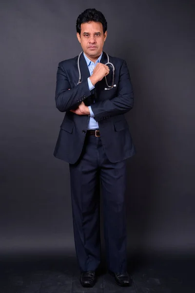 スタジオショットの成熟したハンサムなインドのビジネスマンでスーツとして医師として聴診器で黒の背景 — ストック写真