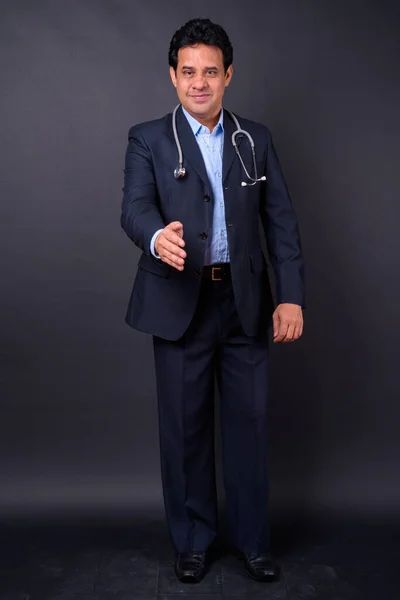 スタジオショットの成熟したハンサムなインドのビジネスマンでスーツとして医師として聴診器で黒の背景 — ストック写真