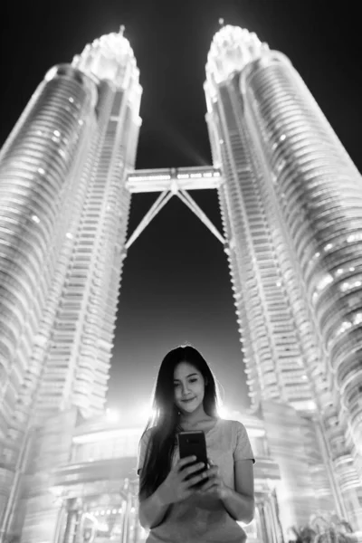 年轻美丽的亚洲女子的画像 与深夜黑白相间的双子塔低角度视图对比 — 图库照片