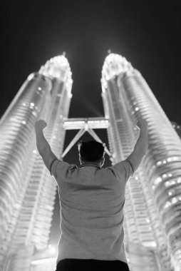 Portrait of young handsome man against low angle view of the Twin Towers at night in black and white