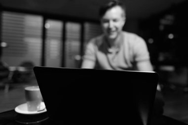 Portrait of young handsome man using laptop in the living room in black and white