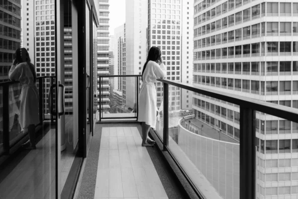 年轻美丽的亚洲女子穿着黑白相间的衣服从阳台上欣赏城市美景的画像 — 图库照片