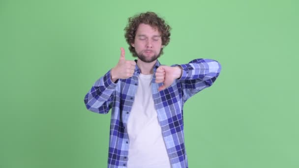 Confuso jovem homem hipster barbudo escolhendo entre polegares para cima e polegares para baixo — Vídeo de Stock