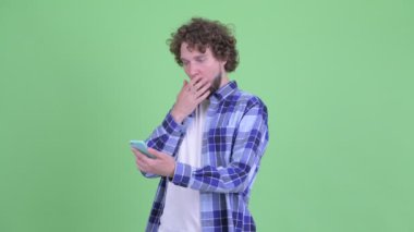 Mutlu genç sakallı hippi telefonu kullanıyor ve şaşırmış görünüyor.
