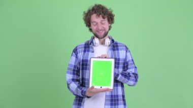 Mutlu genç sakallı hippi dijital tablet gösteriyor.