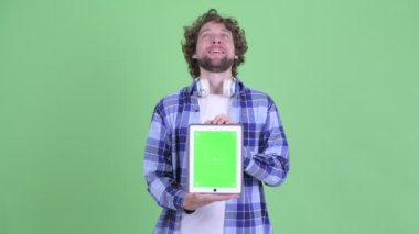 Mutlu genç sakallı hippi dijital tablet gösteriyor ve şaşırmış görünüyor.
